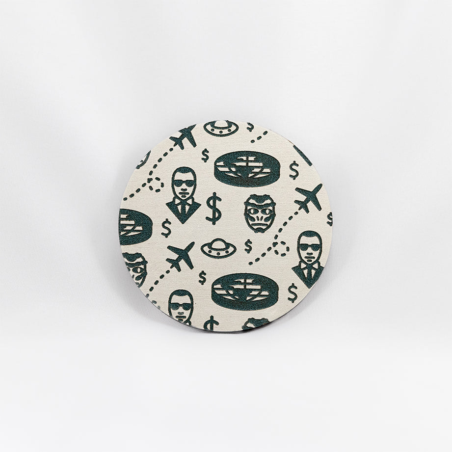 A round white coaster engraved with blue flying saucers, airplanes, a flat earth, dollar signs, a reptilian face, and a man with sunglasses and a black suit on. The coaster is on a white background.