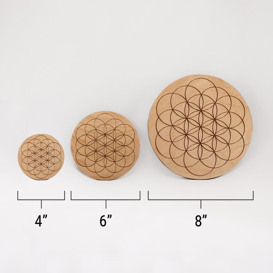Three different sizes of the circular wooden laser-cut crystal grid engraved with the Flower of Life. against a white background with a ruler underneath all three. The smallest measuring 4", the middle 6", and the largest 8".