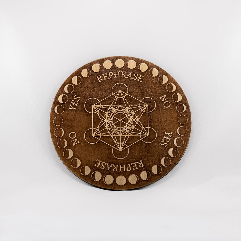 Circular baltic birch laser-cut pendulum board engraved with the words "yes", "no", "rephrase" as well as Metatron's cube and a decorative moon phase border.