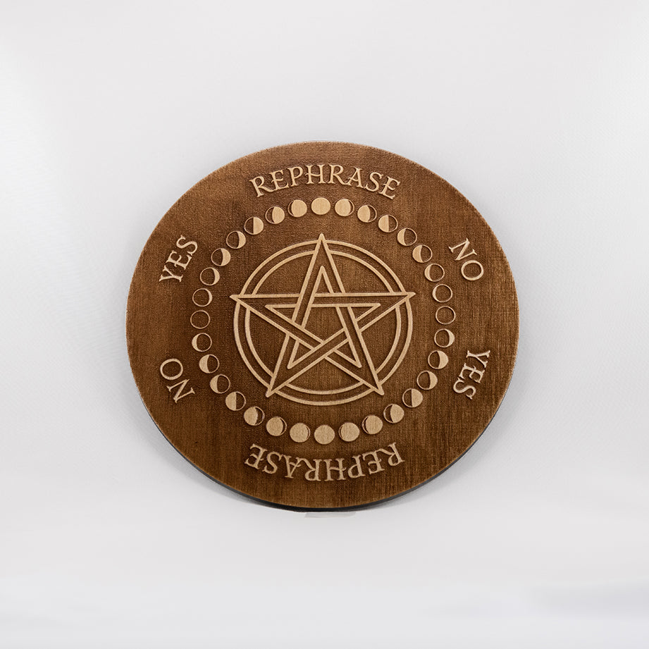 Circular Baltic birch laser-cut pendulum board engraved around its border with the words "yes", "no", "rephrase", the board has a pentacle in the centre encircled with the different moon phases.