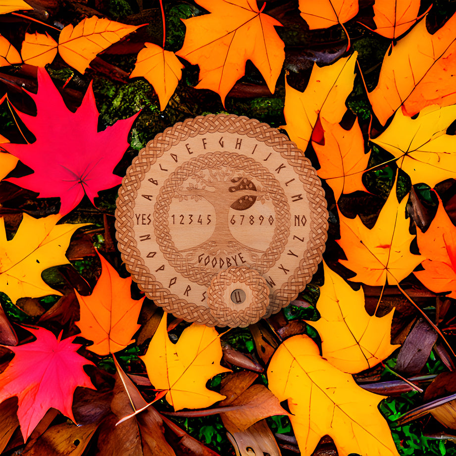 Circular Baltic birch laser-cut spirit board engraved with the words "yes", "no", "goodbye", as well as the entire alphabet lays on the leaf covered ground. The board has the Tree of Life in the centre and a decorative die-cut braid border. A small circular planchette with a die-cut edge sits on top of the board.