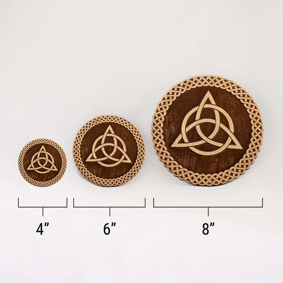 Three different sizes of the circular wooden laser-cut crystal grid engraved with the Celtic Triquetra symbol and a scalloped braid border against a white background with a ruler underneath all three. The smallest measuring 4", the middle 6", and the largest 8".