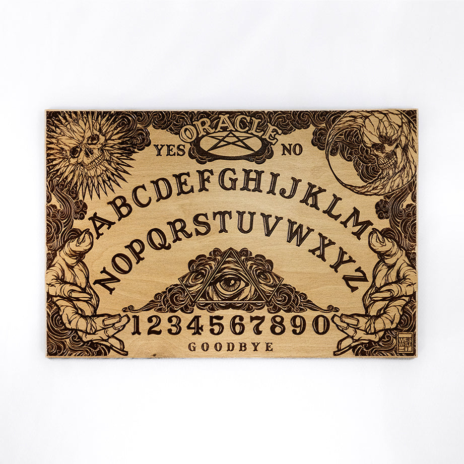 A rectangular wooden laser-cut spirit board engraved with the alphabet and numbers 0-9, yes, no, and goodbye. A sun with a skull face is engraved in the top left corner, a moon with a skull face is engraved in the top right corner, the bottom left and right corners are decorated with outstretched hands. The board is on a plain white background.