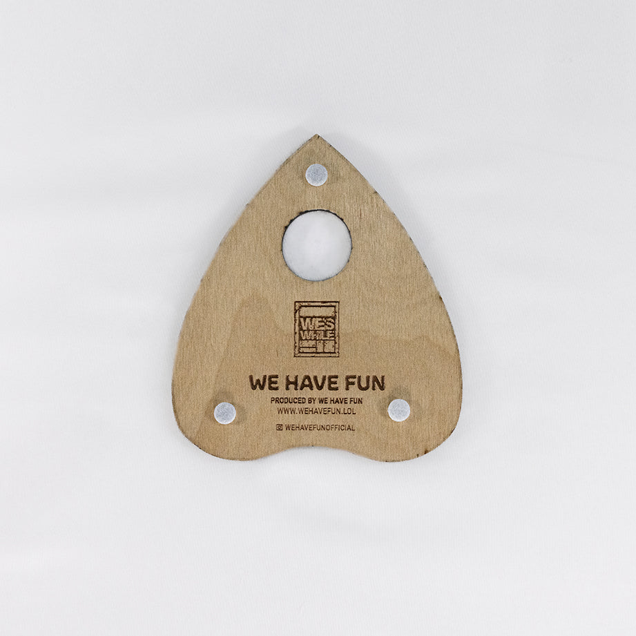 The back of the wooden planchette on a plain white background. The planchette is engraved with the artist Wes While's logo, "We Have Fun", "www.wehavefun.lol", and We Have Fun instagram link "wehavefunofficial". The planchette has 3 felt pads for easy sliding on the board.