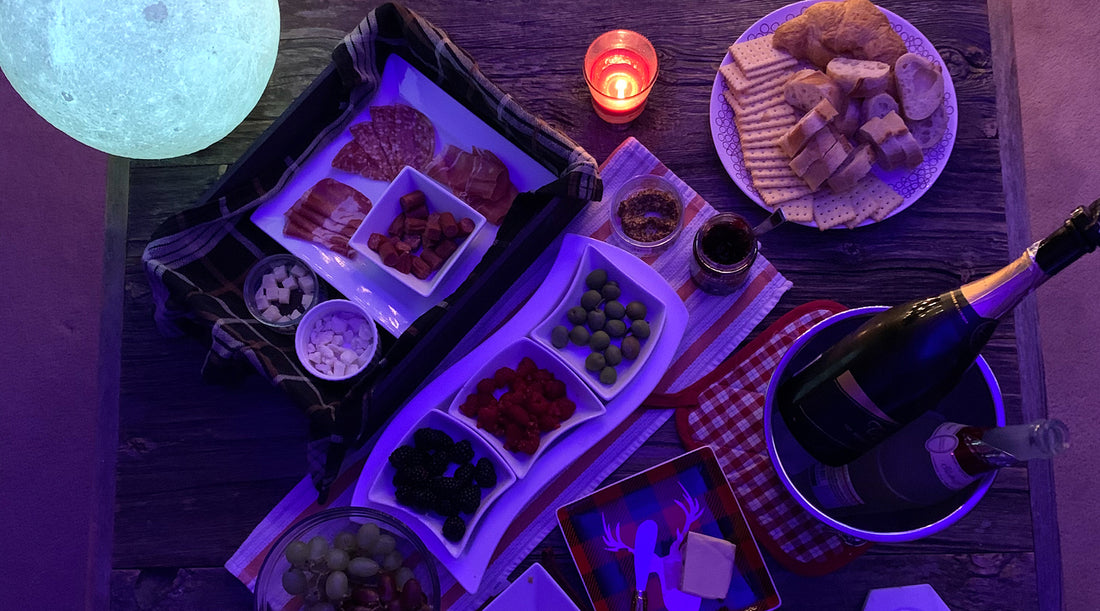 A charcuterie board of cheese, meat, bread, grapes, and olives, with sparkling wine on a wooden table.