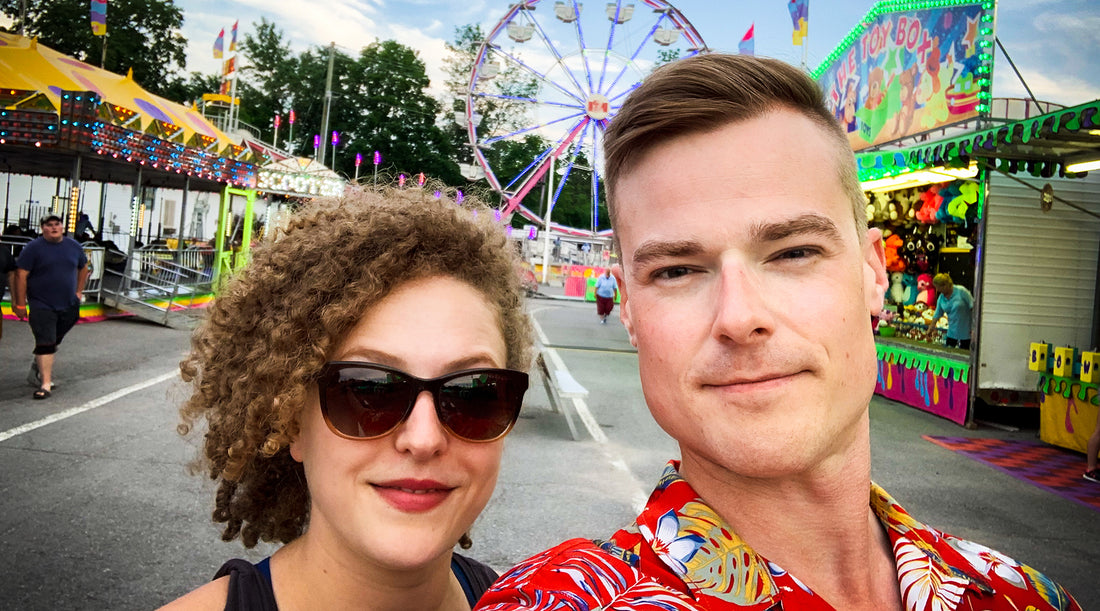 Creators of the blog Danielle, a blonde woman, and Kris, a blonde man smile in front of a ferris wheel at a midway