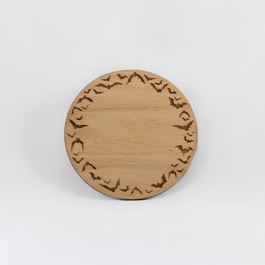 A circular wooden laser-cut crystal grid engraved with a border made up of bats in flight with a plain white background.