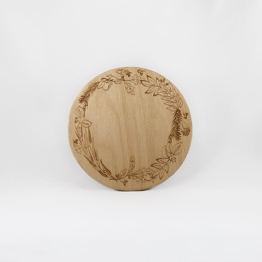 A circular wooden laser-cut crystal grid engraved with a border made up of Apple, Yew, Hazel, Edler, Elm, Willow, Oak, Alder, and Ash tree branches with a plain white background. 