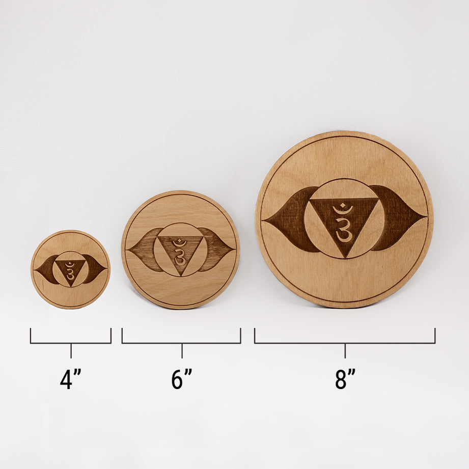 Three different sizes of the circular wooden laser-cut crystal grid engraved with the third eye chakra symbol against a white background with a ruler underneath all three. The smallest measuring 4", the middle 6", and the largest 8".