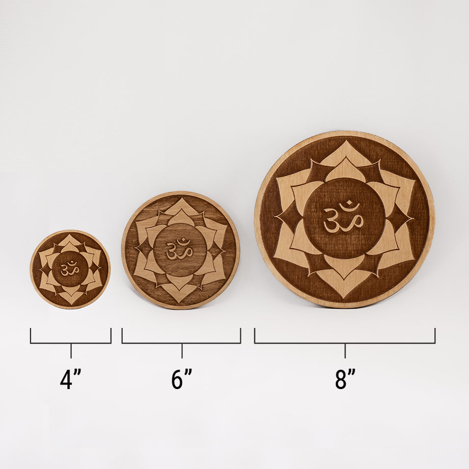 Three different sizes of the circular wooden laser-cut crystal grid engraved with the crown chakra symbol against a white background with a ruler underneath all three. The smallest measuring 4", the middle 6", and the largest 8".