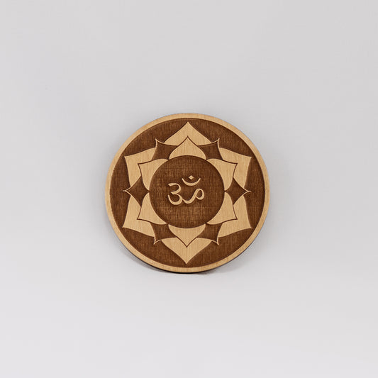 A circular wooden laser-cut crystal grid engraved with the crown chakra symbol with a plain white background.