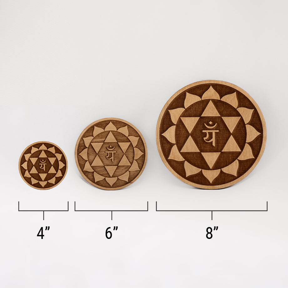 Three different sizes of the circular wooden laser-cut crystal grid engraved with the heart chakra symbol against a white background with a ruler underneath all three. The smallest measuring 4", the middle 6", and the largest 8".