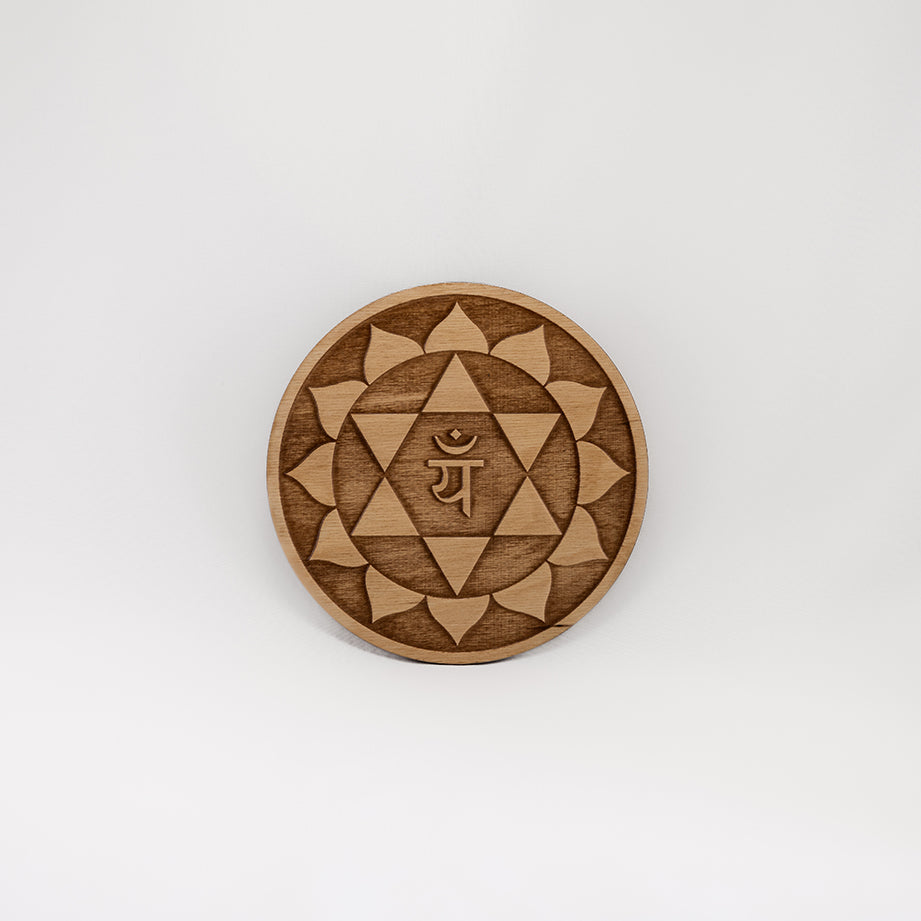 A circular wooden laser-cut crystal grid engraved with the heart chakra symbol with a plain white background. 