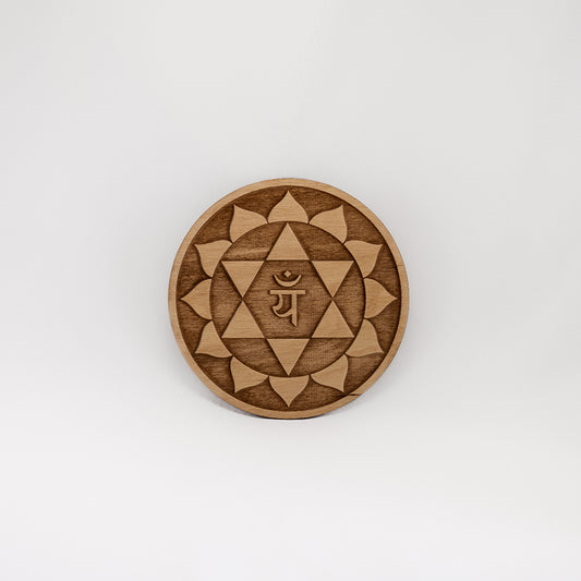 A circular wooden laser-cut crystal grid engraved with the heart chakra symbol with a plain white background. 