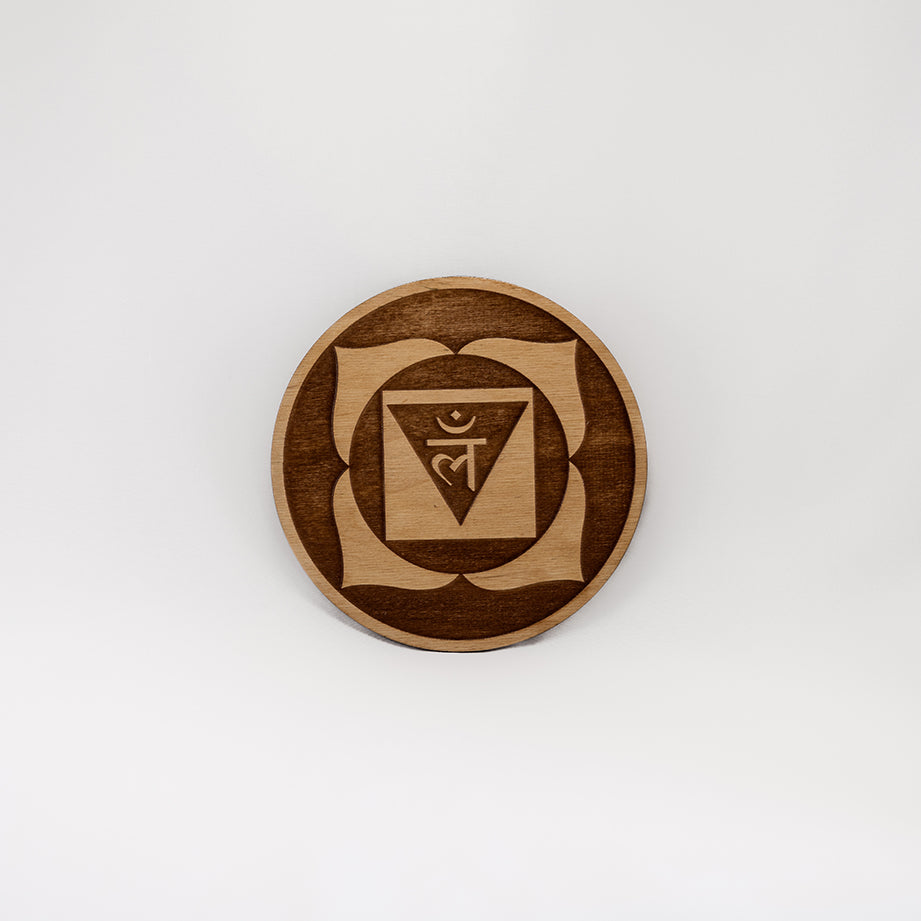 A circular wooden laser-cut crystal grid engraved with the root chakra symbol with a plain white background. 