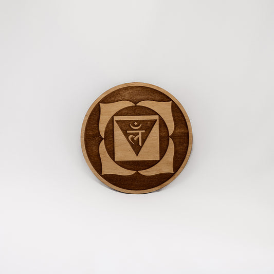 A circular wooden laser-cut crystal grid engraved with the root chakra symbol with a plain white background. 