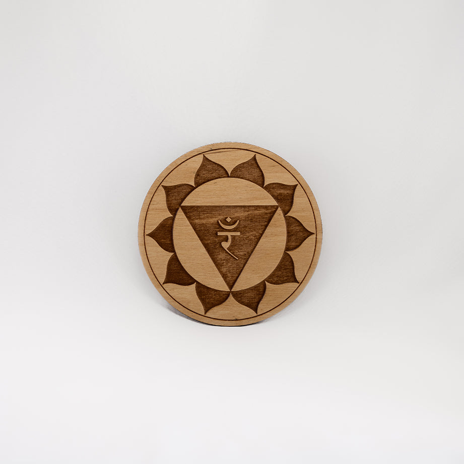 A circular wooden laser-cut crystal grid engraved with the solar plexus chakra symbol with a plain white background. 