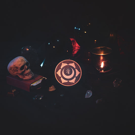 A circular wooden laser-cut crystal grid engraved with the sacral chakra symbol. The grid sits amongst candles, crystal balls, a skull, tarot cards and assorted crystals.