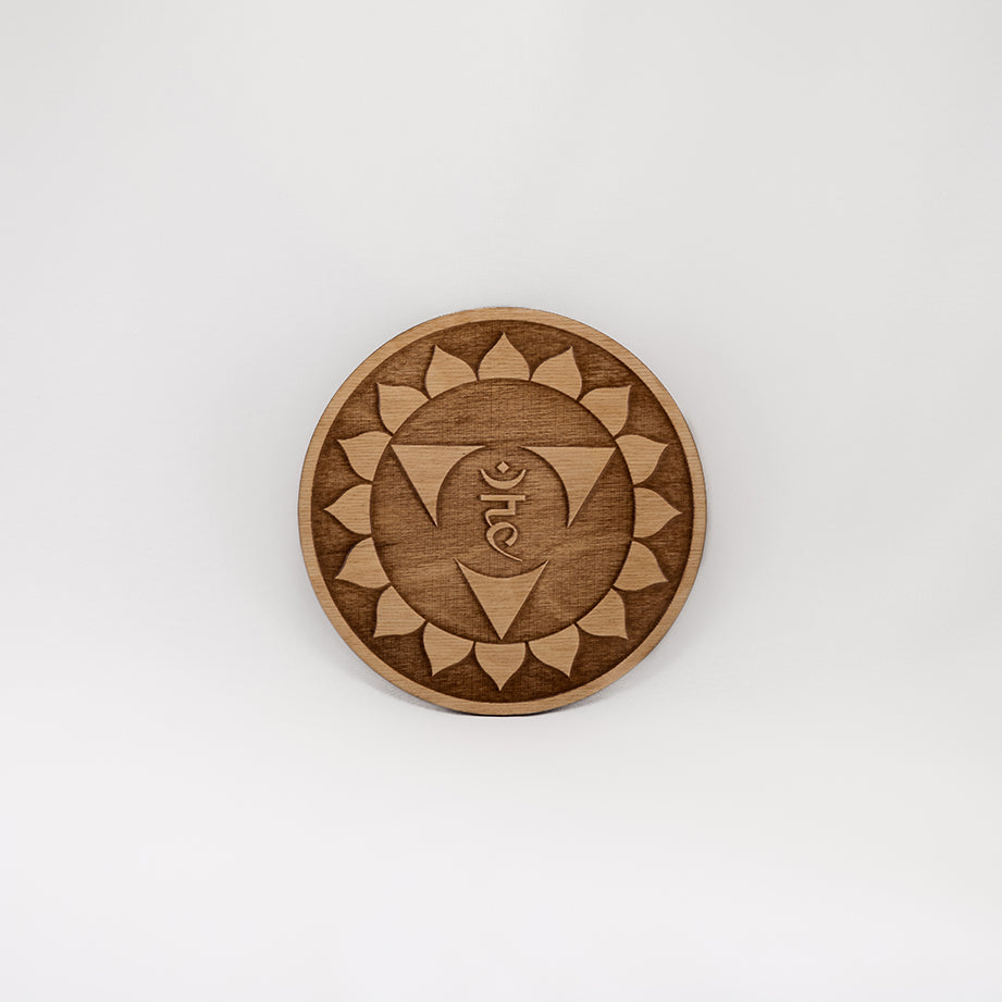 A circular wooden laser-cut crystal grid engraved with the throat chakra symbol with a plain white background. 