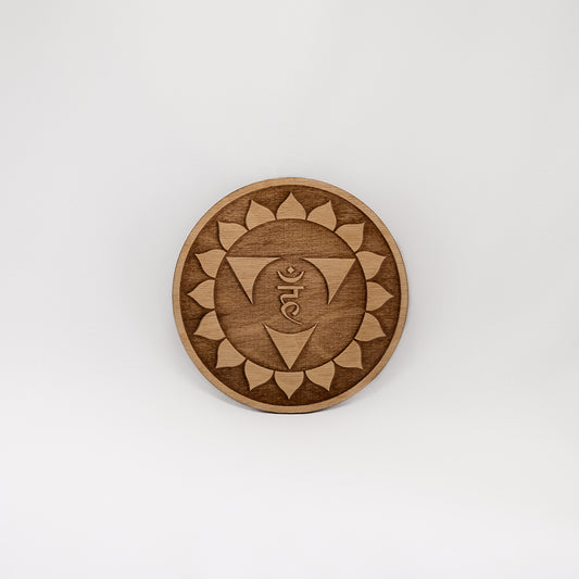 A circular wooden laser-cut crystal grid engraved with the throat chakra symbol with a plain white background.