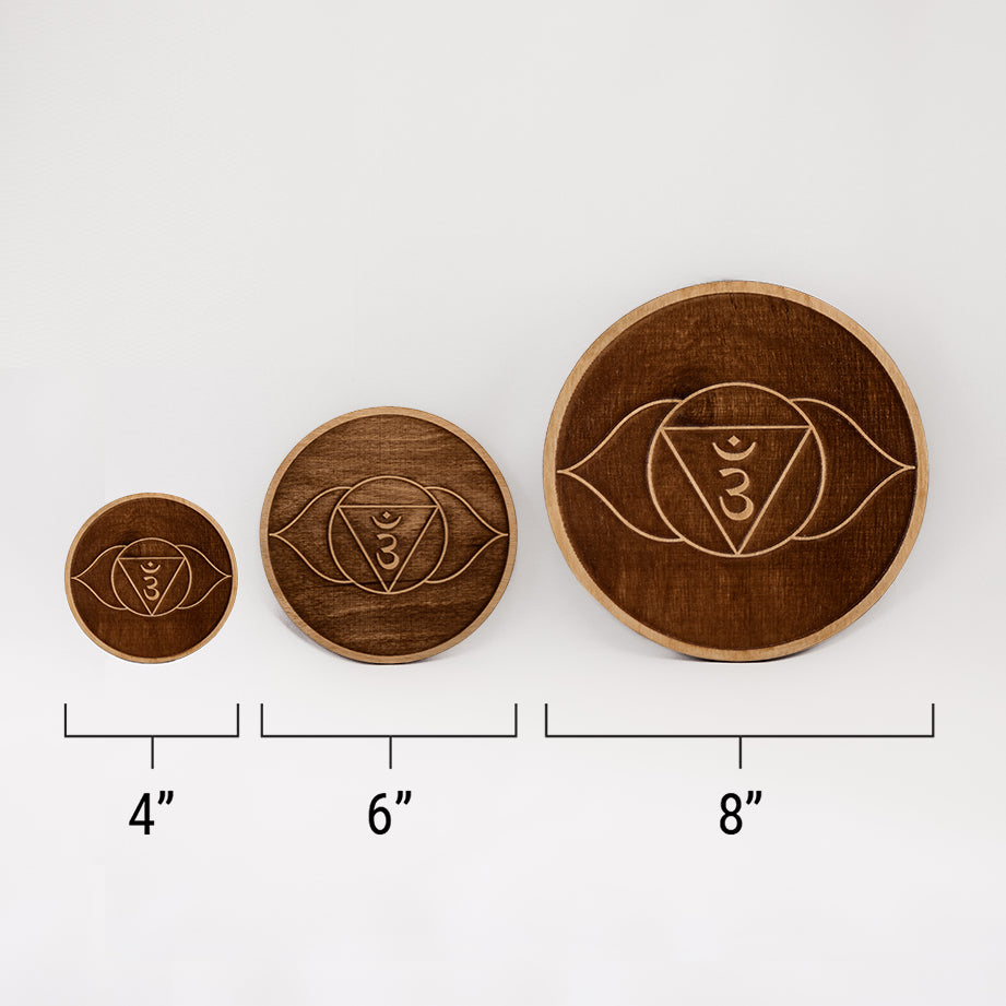 Three different sizes of the circular wooden laser-cut crystal grid engraved with the third eye chakra symbol against a white background with a ruler underneath all three. The smallest measuring 4", the middle 6", and the largest 8".