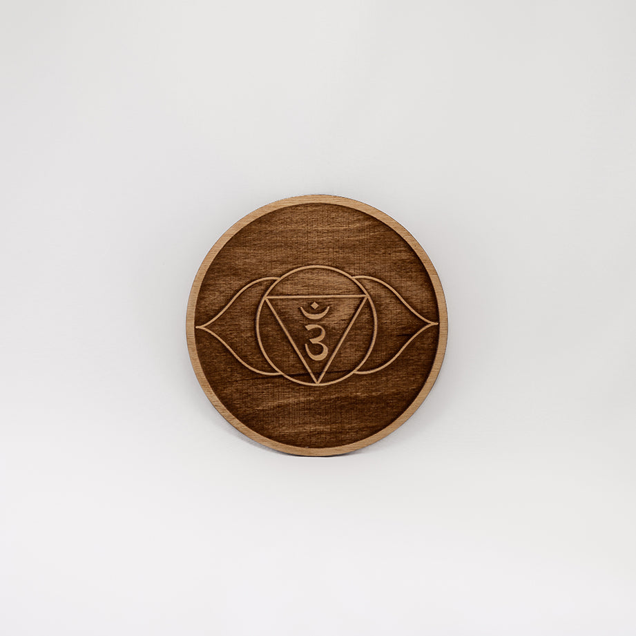 A circular wooden laser-cut crystal grid engraved with the third eye chakra symbol with a plain white background. 