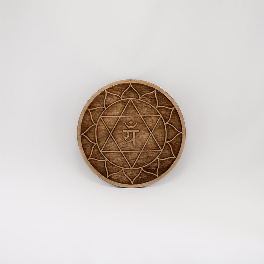 A circular wooden laser-cut crystal grid engraved with the heart chakra symbol with a plain white background. 