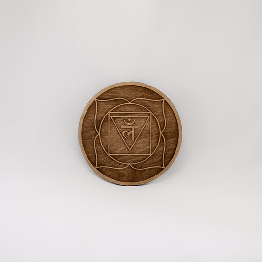 A circular wooden laser-cut crystal grid engraved with the root chakra symbol with a plain white background. 