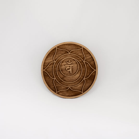 A circular wooden laser-cut crystal grid engraved with the sacral chakra symbol with a plain white background. 