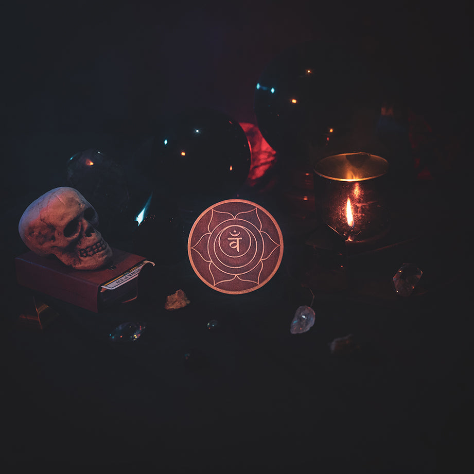 A circular wooden laser-cut crystal grid engraved with the sacral chakra symbol. The grid sits amongst candles, crystal balls, a skull, tarot cards and assorted crystals.