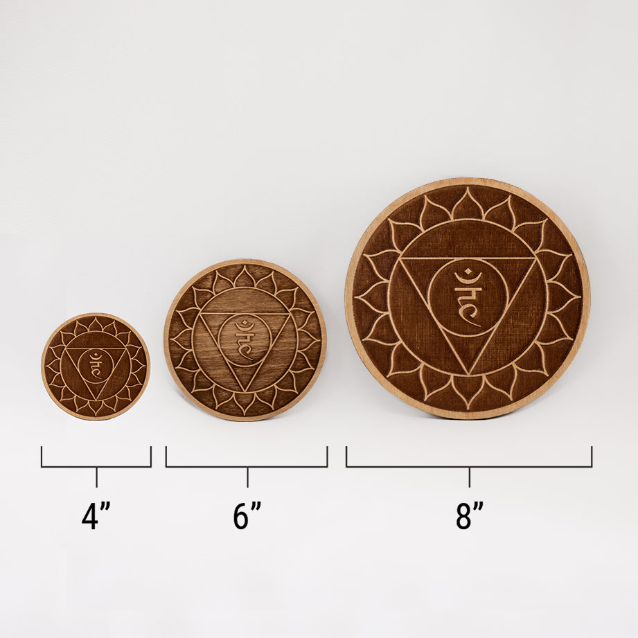 Three different sizes of the circular wooden laser-cut crystal grid engraved with the throat chakra symbol against a white background with a ruler underneath all three. The smallest measuring 4", the middle 6", and the largest 8".