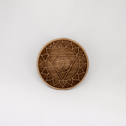 A circular wooden laser-cut crystal grid engraved with the throat chakra symbol with a plain white background. 