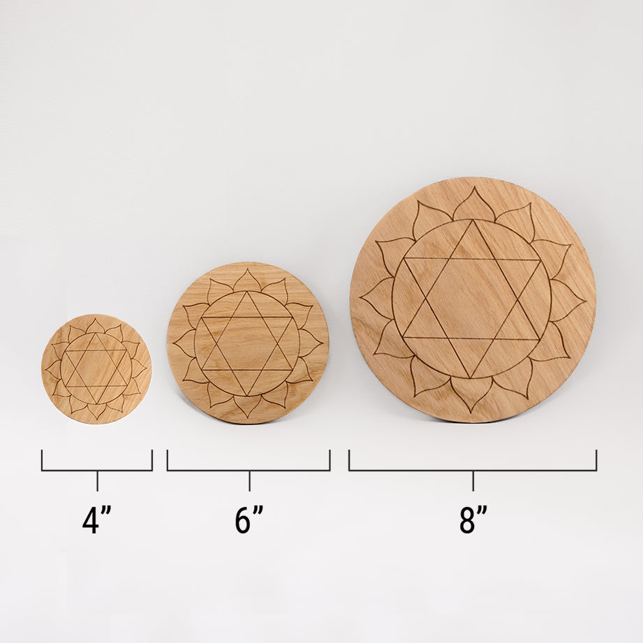 Three different sizes of the circular wooden laser-cut crystal grid engraved with the heart chakra symbol against a white background with a ruler underneath all three. The smallest measuring 4", the middle 6", and the largest 8".