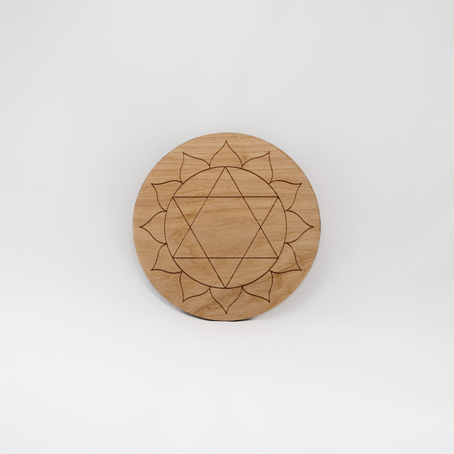 A circular wooden laser-cut crystal grid engraved with the heart chakra symbol with a plain white background. 