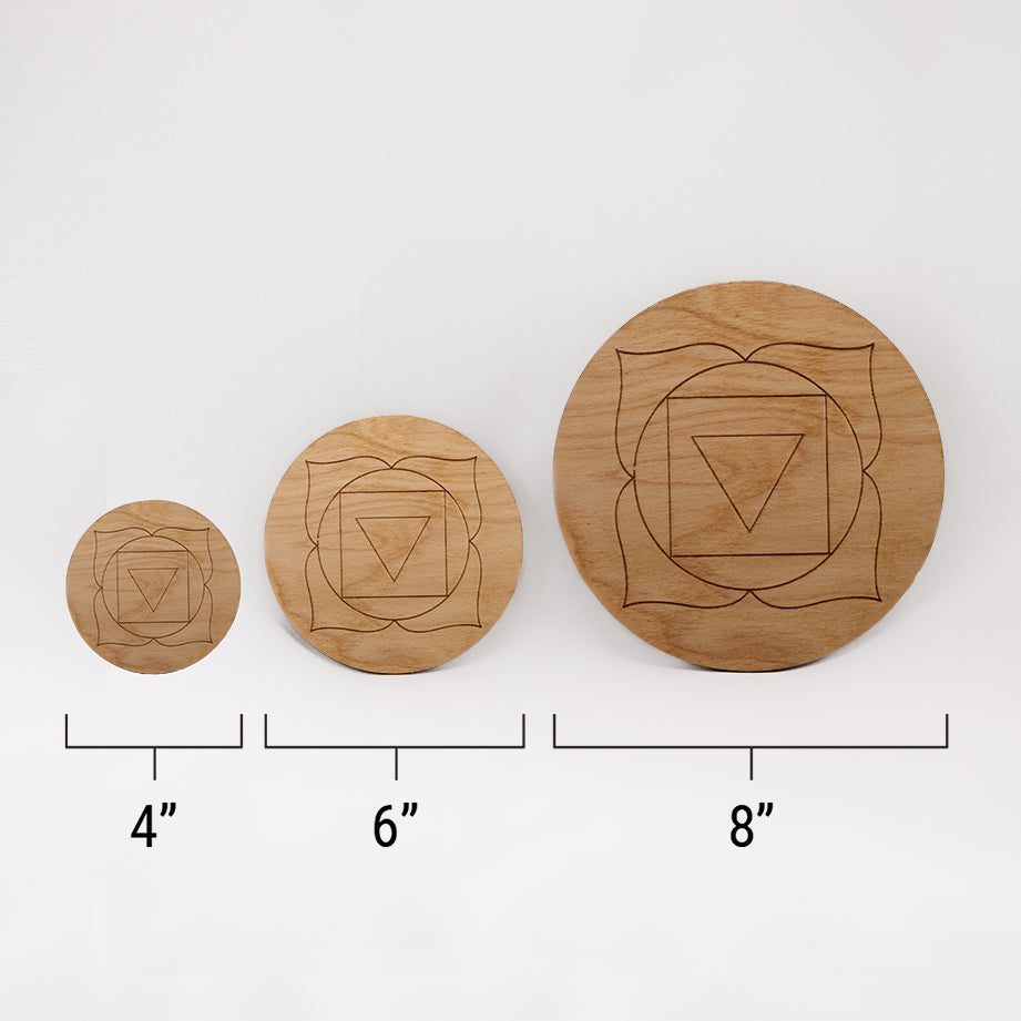 Three different sizes of the circular wooden laser-cut crystal grid engraved with the root chakra symbol against a white background with a ruler underneath all three. The smallest measuring 4", the middle 6", and the largest 8".