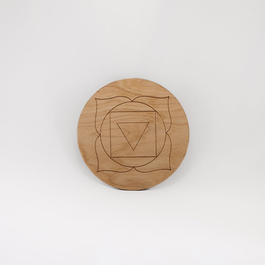 A circular wooden laser-cut crystal grid engraved with the root chakra symbol with a plain white background. 