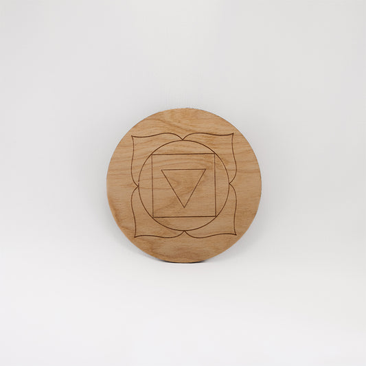 A circular wooden laser-cut crystal grid engraved with the root chakra symbol with a plain white background.