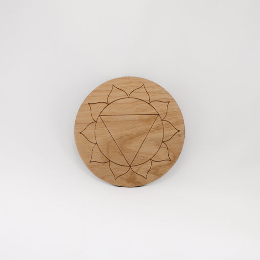 A circular wooden laser-cut crystal grid engraved with the solar plexus chakra symbol with a plain white background. 