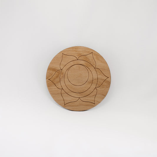 A circular wooden laser-cut crystal grid engraved with the sacral chakra symbol with a plain white background. 