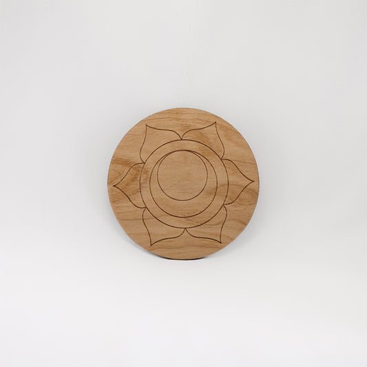 A circular wooden laser-cut crystal grid engraved with the sacral chakra symbol with a plain white background.