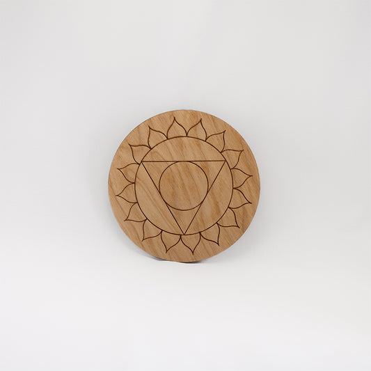 A circular wooden laser-cut crystal grid engraved with the throat chakra symbol with a plain white background. 