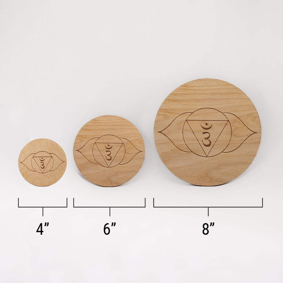 Three different sizes of the circular wooden laser-cut crystal grid engraved with the third eye chakra symbol against a white background with a ruler underneath all three. The smallest measuring 4", the middle 6", and the largest 8".