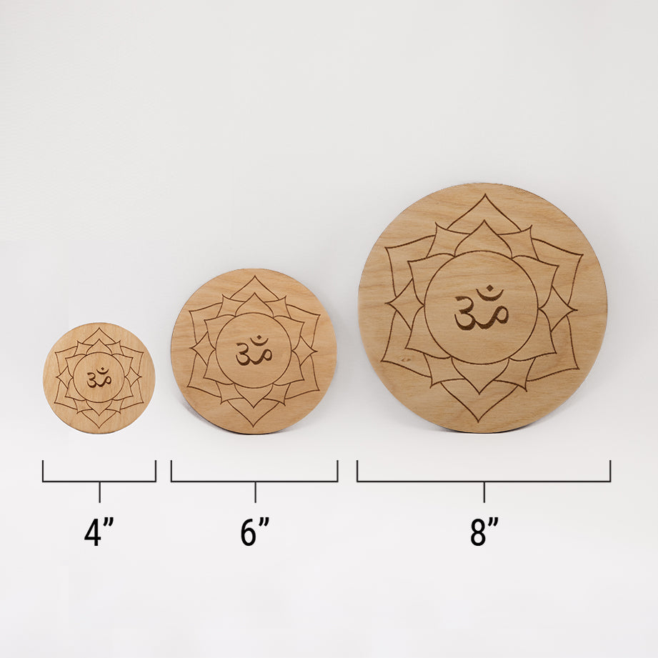 Three different sizes of the circular wooden laser-cut crystal grid engraved with the crown chakra symbol against a white background with a ruler underneath all three. The smallest measuring 4", the middle 6", and the largest 8".