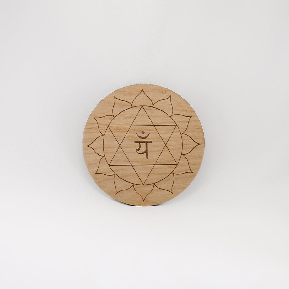 A circular wooden laser-cut crystal grid engraved with the heart chakra symbol with a plain white background. 