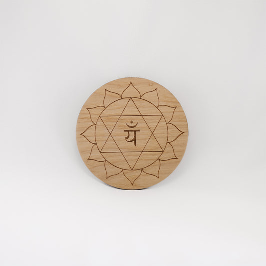 A circular wooden laser-cut crystal grid engraved with the heart chakra symbol with a plain white background. 