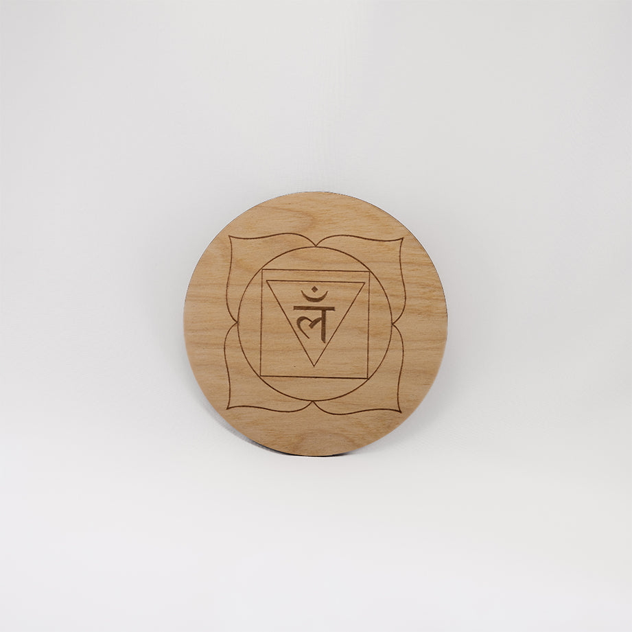 A circular wooden laser-cut crystal grid engraved with the root chakra symbol with a plain white background. 