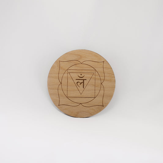 A circular wooden laser-cut crystal grid engraved with the root chakra symbol with a plain white background. 