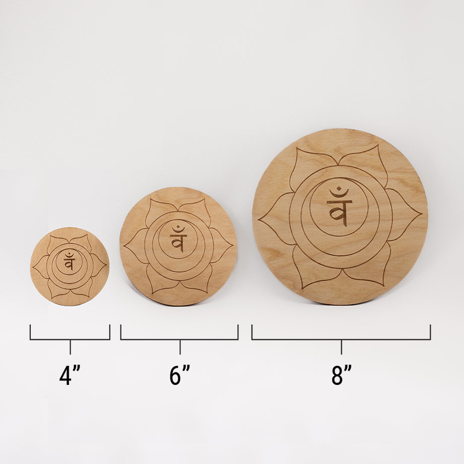 Three different sizes of the circular wooden laser-cut crystal grid engraved with the sacral chakra symbol against a white background with a ruler underneath all three. The smallest measuring 4", the middle 6", and the largest 8".