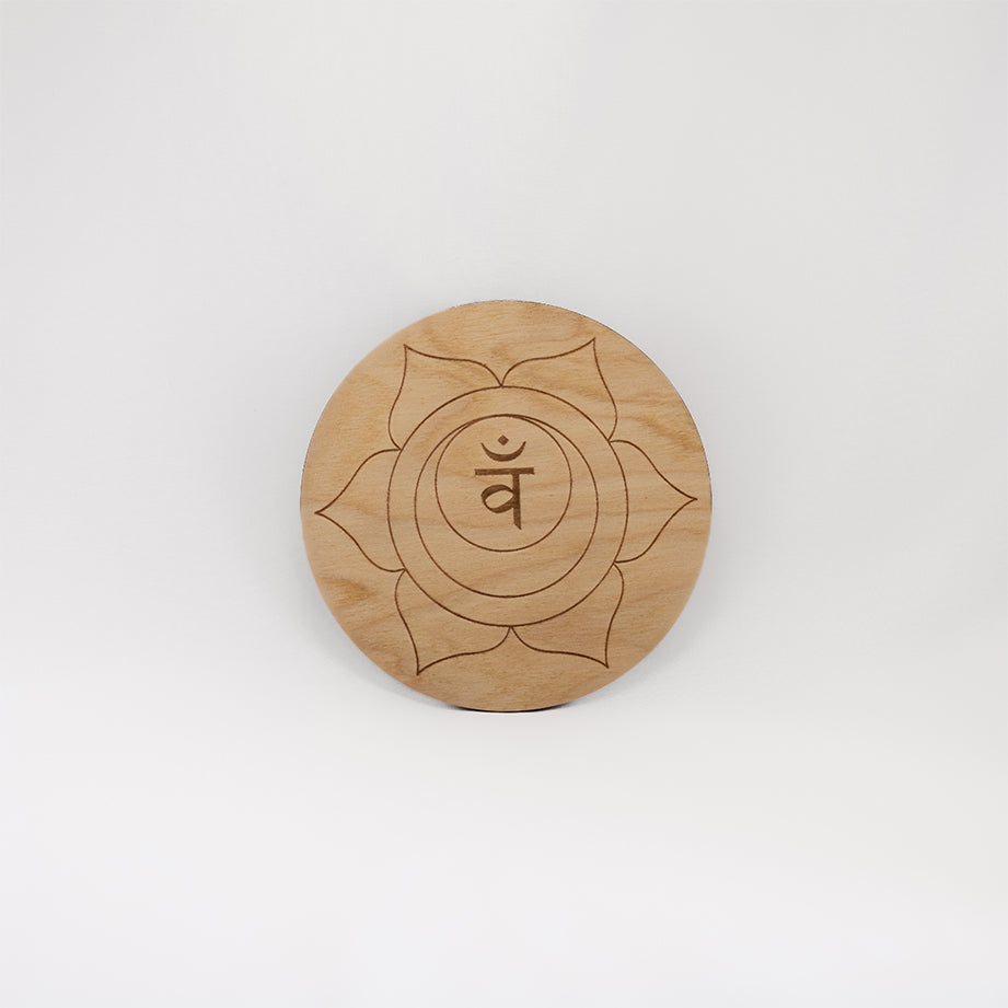 A circular wooden laser-cut crystal grid engraved with the sacral chakra symbol with a plain white background. 