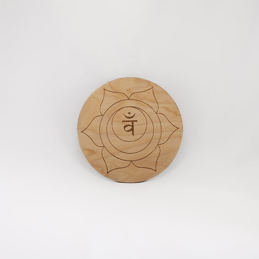 A circular wooden laser-cut crystal grid engraved with the sacral chakra symbol with a plain white background. 